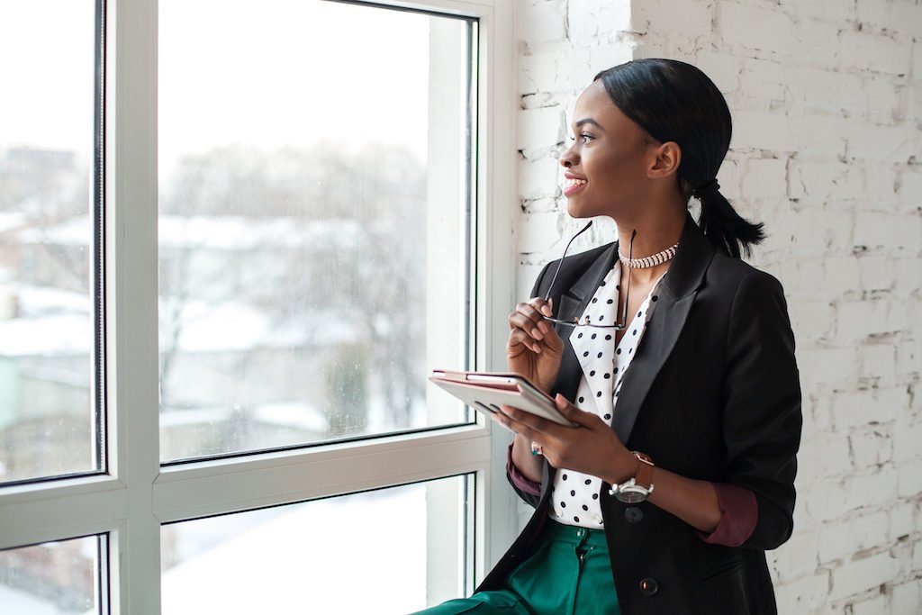 A woman dressed professionally looking out a window and smiling.
