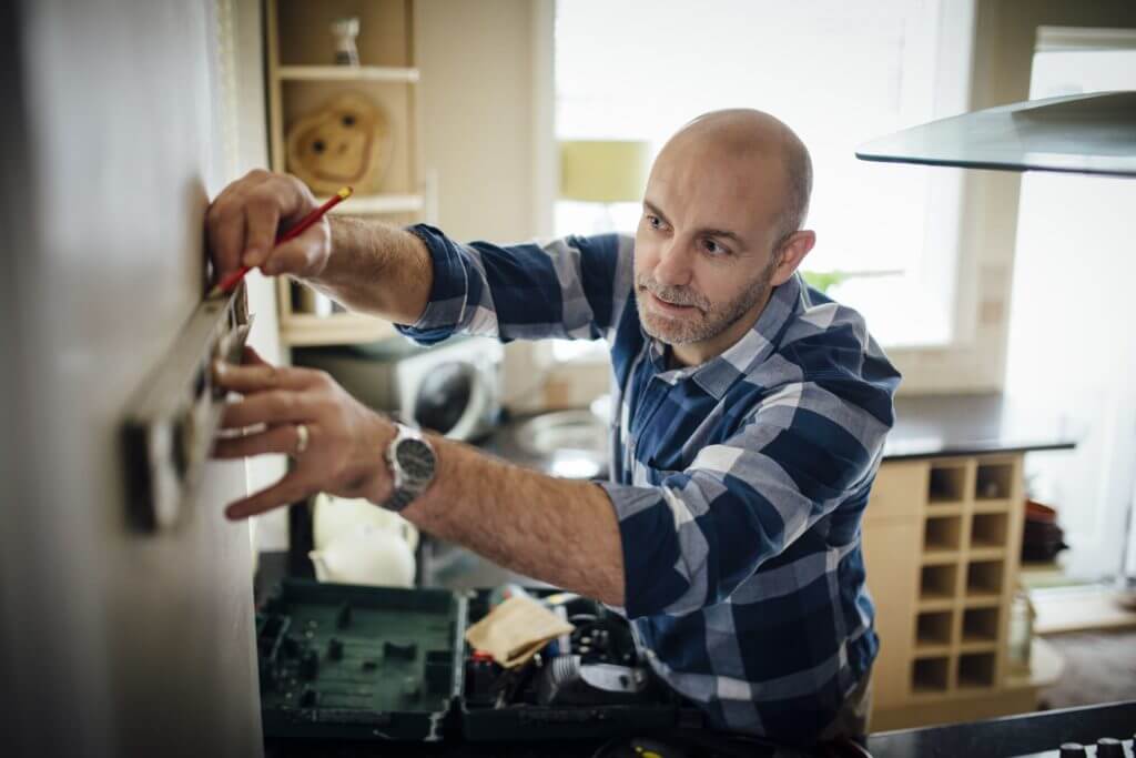 A man in plaid doing renovations in his home and concentrating on them.