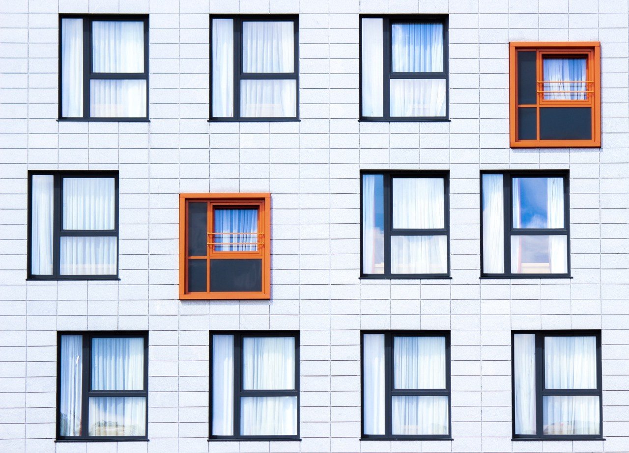 An apartment complex of white brick and many windows and one orange one.