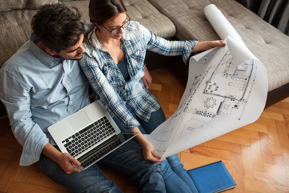 Two people looking at a house plan while sitting on the ground with a laptop.