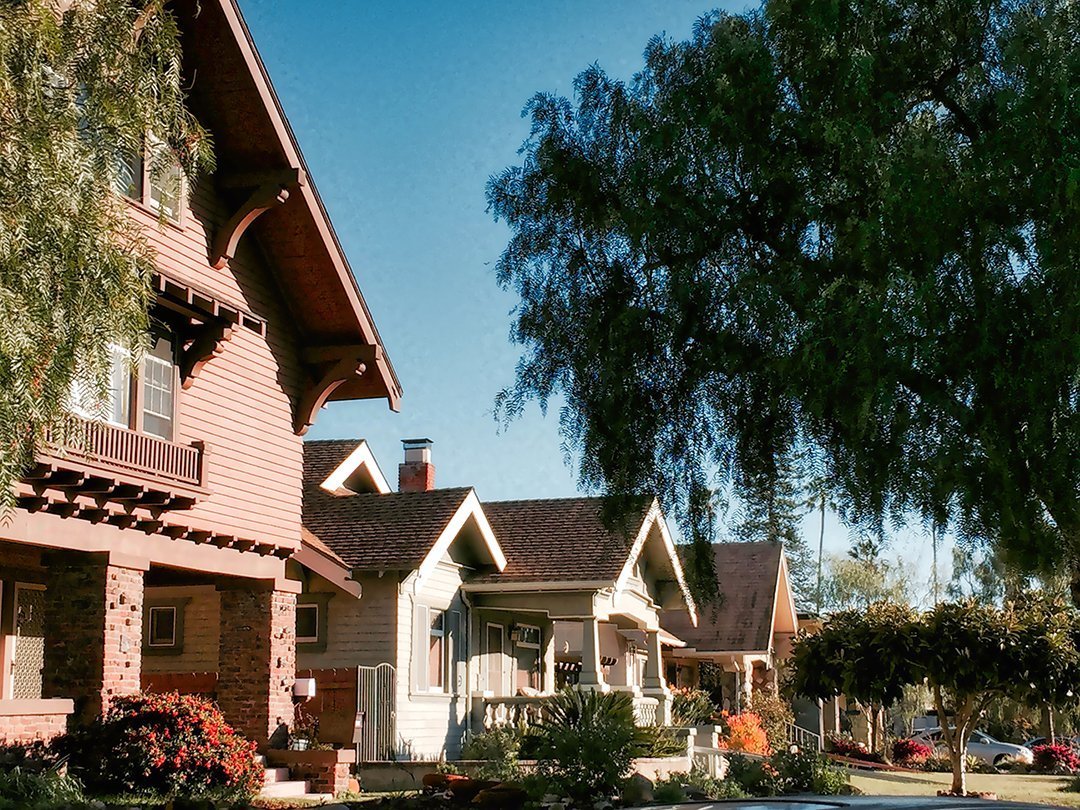 A street of houses lined up with a big tree off to the side.