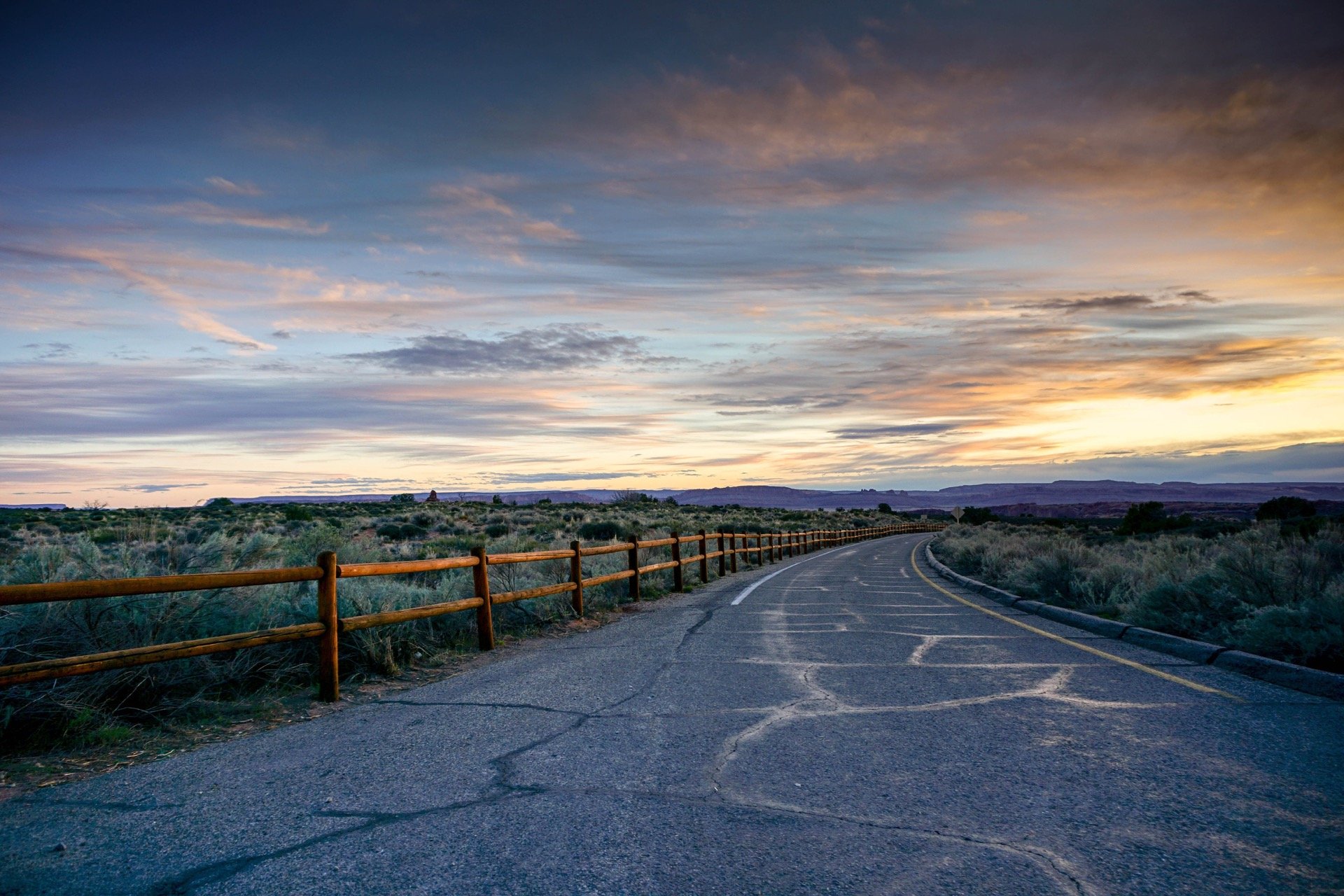 A long road with a fence at sunset and country background.