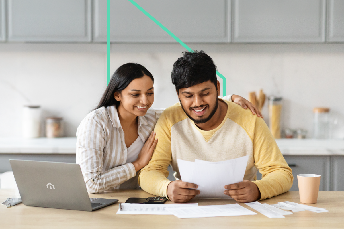 Two real estate investors smile while reviewing Kiavi bridge loan documents at a kitchen table, a laptop and coffee cup nearby.