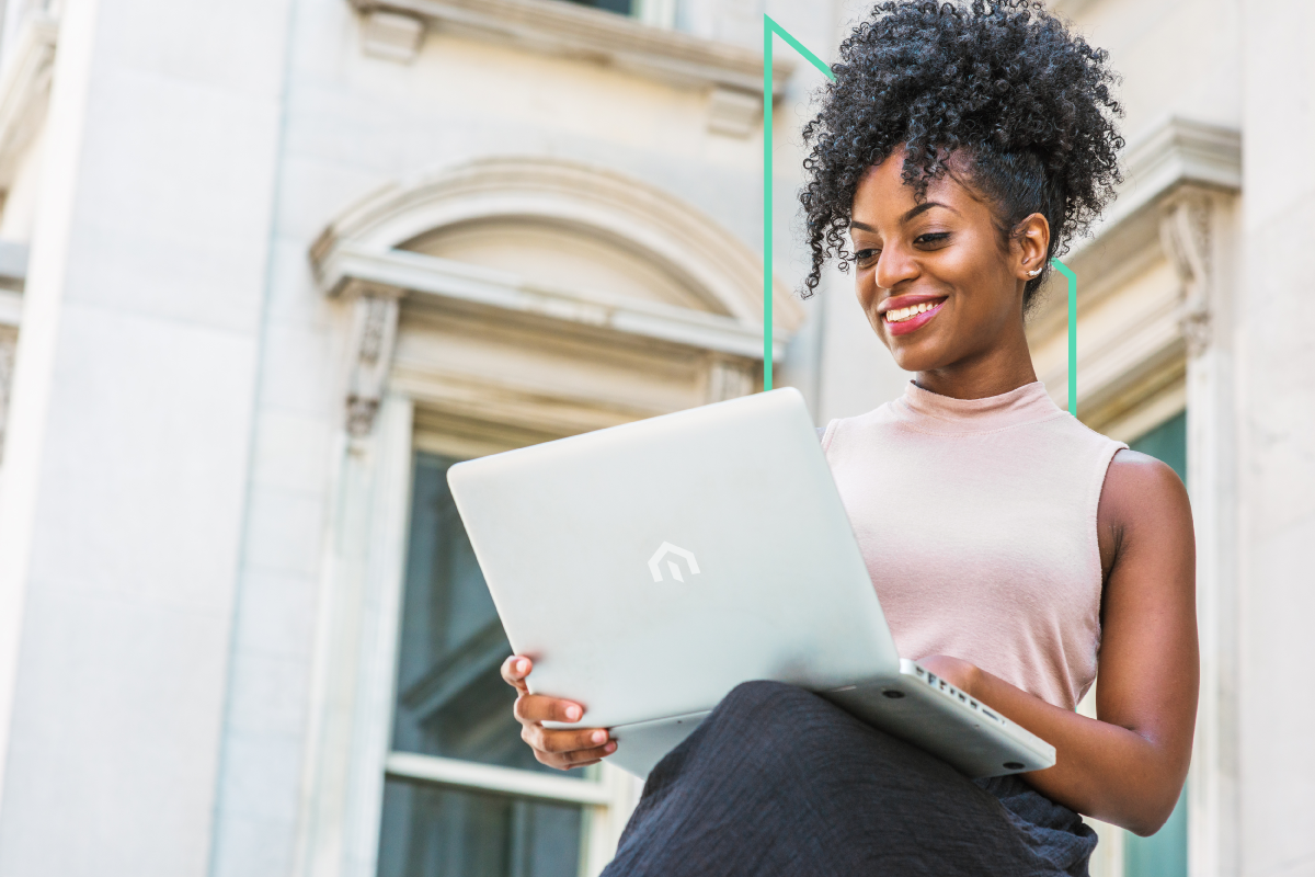 A real estate investor with curly hair sits outdoors, smiling while analyzing opportunities on her laptop.