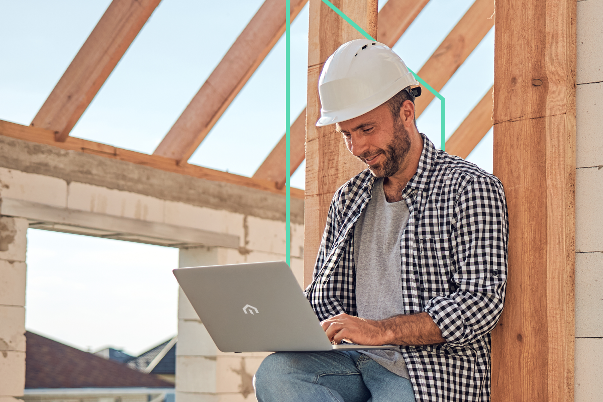 A Kiavi real estate investor in a hard hat sitting at a construction site with a laptop, smiling and managing their next project.