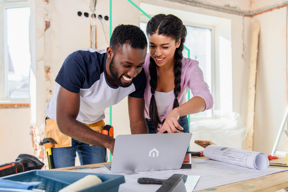 A real estate investor and contractor review plans on a laptop at a construction site, surrounded by blueprints.