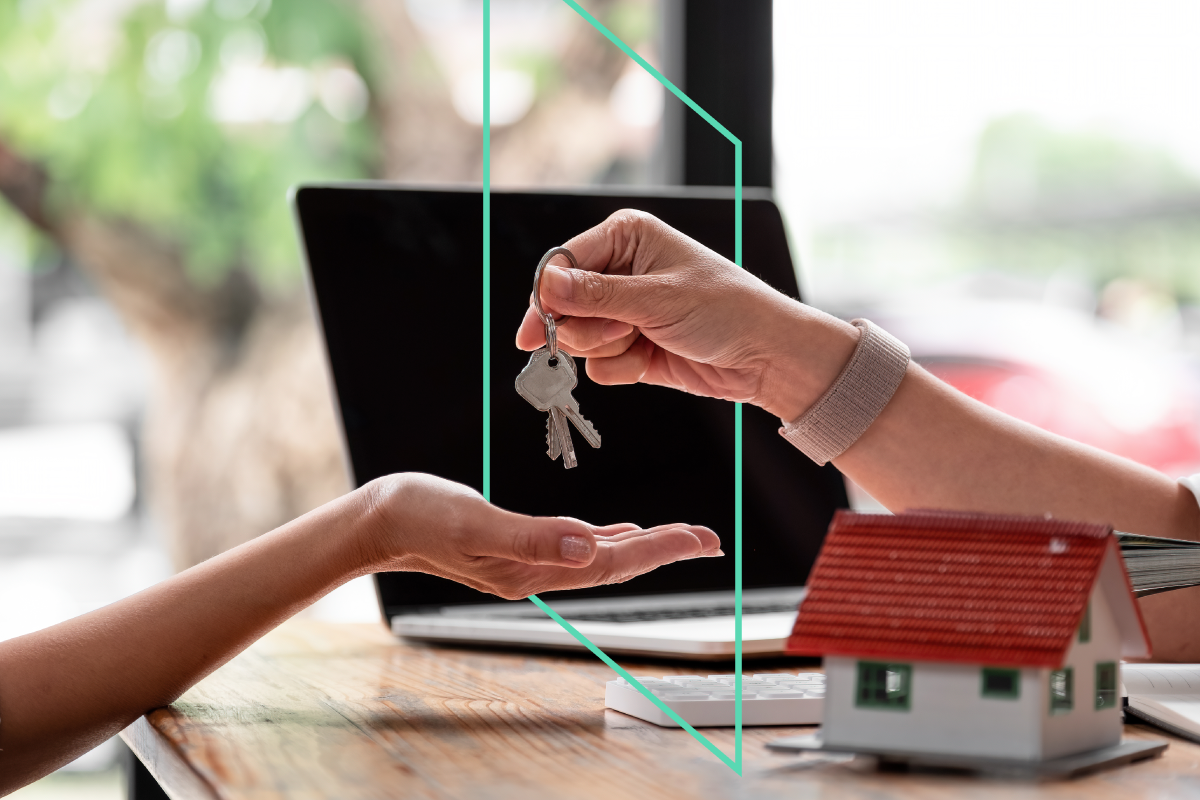 Real estate agent passes keys to a real estate investor who has just purchased a property with help from Kiavi. A small house and a laptop are in the background.