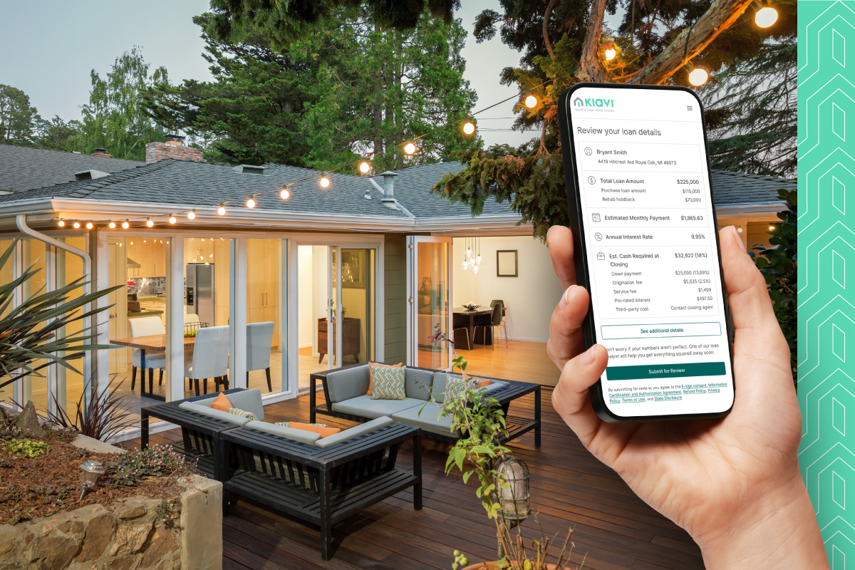 A real estate investor reviews Kiavi loan details on their phone while standing in front of a patio with a seating area and a kitchen visible through glass doors.