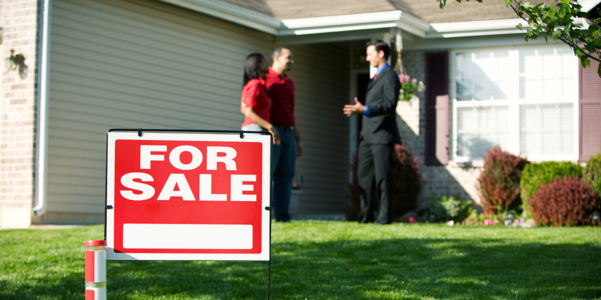 real estate agent meeting with potential buyers in front of a house with a for sale sign in front