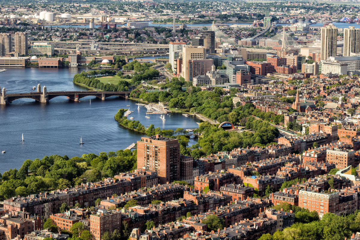 Aerial view of Boston's Charles River, buildings, and green parks with boats on the water. 