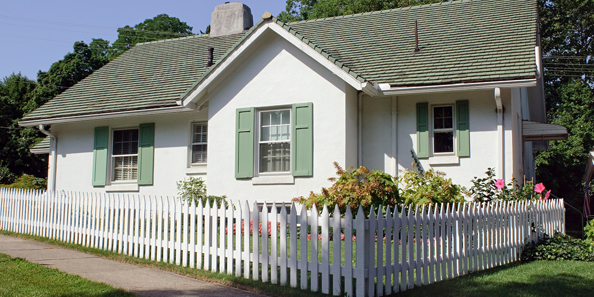 A white rental property with green shutters and a white picket fence