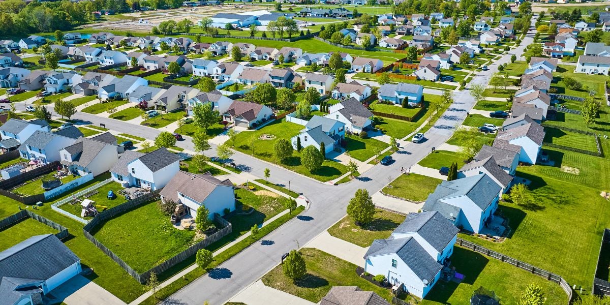 Aerial view of a suburban neighborhood with a patchwork of single-family properties, lush green lawns, and intersecting streets on a bright sunny day.
