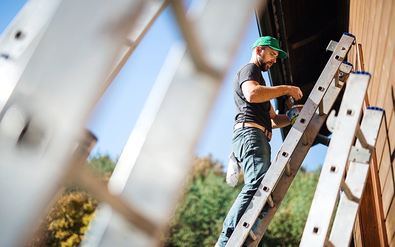 A real estate investor standing on a ladder painting his new fix-and-flip property