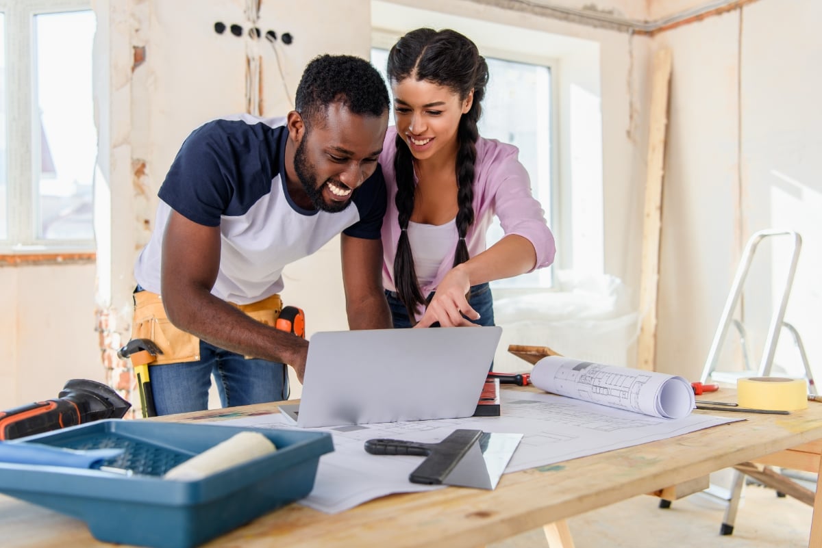 Two real estate investors working on their fix-and-flip investment property by reviewing blueprints on their laptop