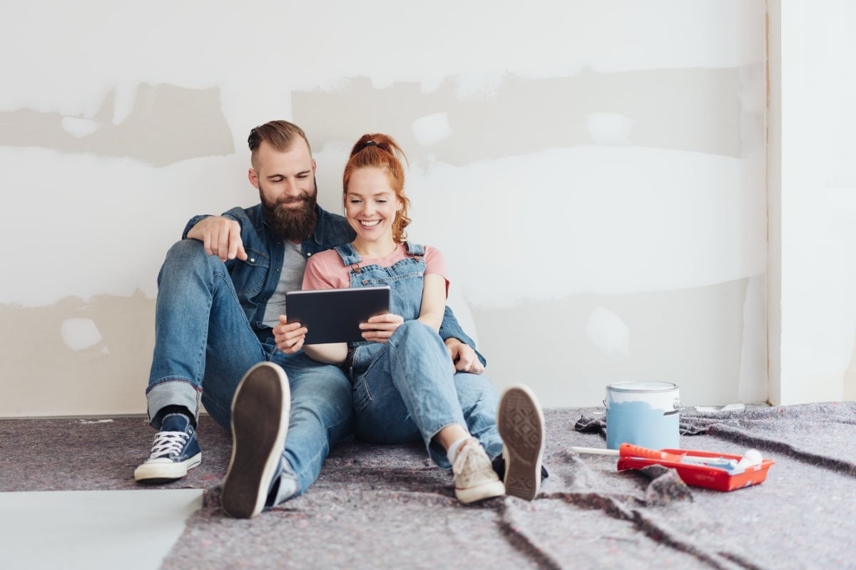 Two real estate investors reviewing project plans for their fix-and-flip investment on a tablet while sitting on the floor