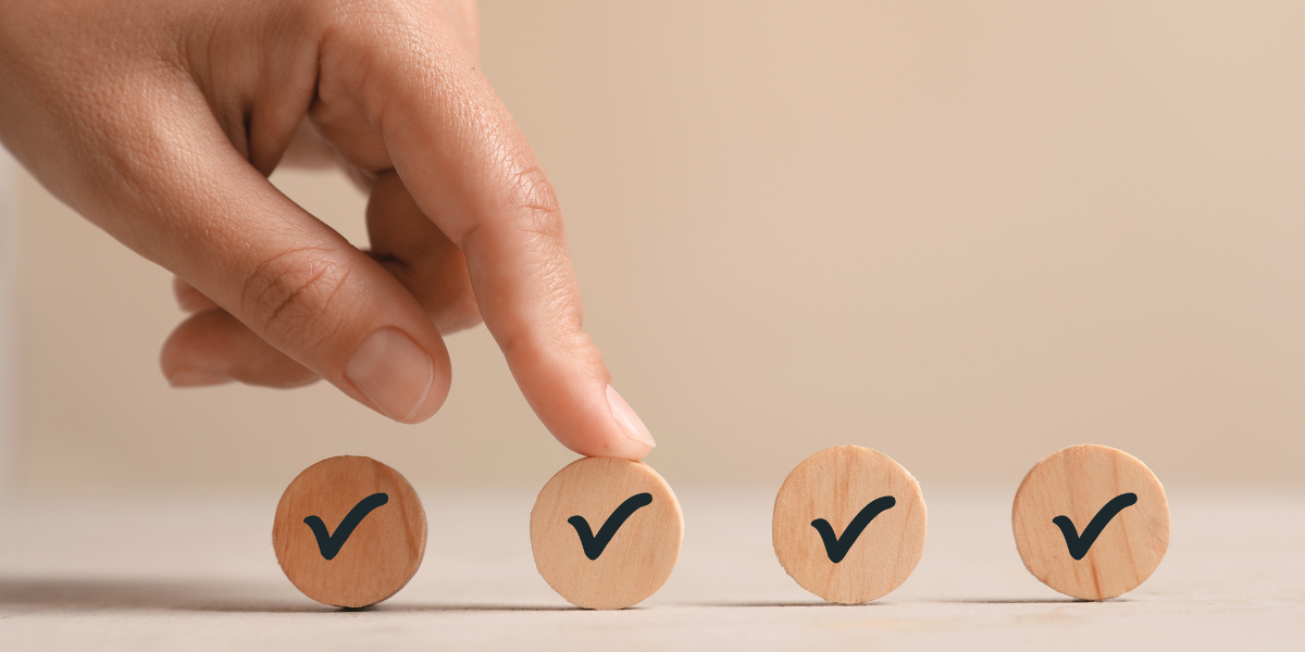 A close-up of a person's hand pointing at one of four wooden circular blocks, each marked with a black checkmark, suggesting a real estate agent is selecting a financing option for a fix-and-flip property with Kiavi.