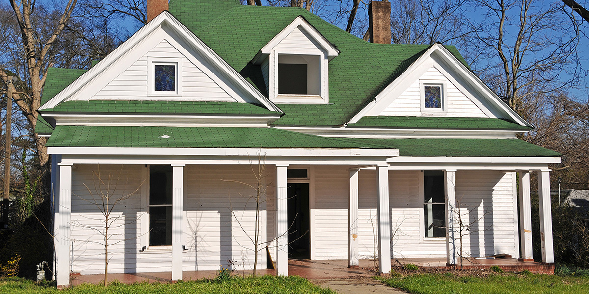 A white fixer upper house with a green roof